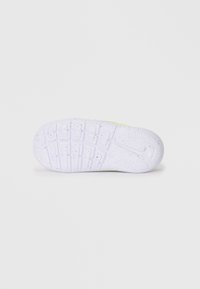 Semelle de chaussure en caoutchouc blanc avec une surface texturée et à motif, ornée de taches noires et d'un design de logo distinctif.