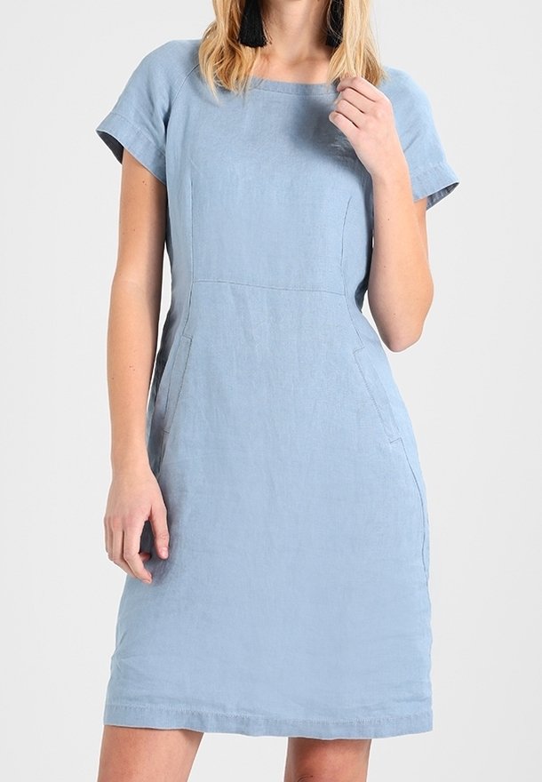 Femme portant une robe bleu clair mi-longue, manches courtes, avec un col carré et des détails subtils de coutures.