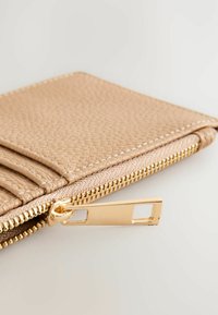 Beige kožená peněženka s texturovaným povrchem, několika přihrádkami na karty a zlatým zipem. Ozdobená bílým prošíváním na okrajích.