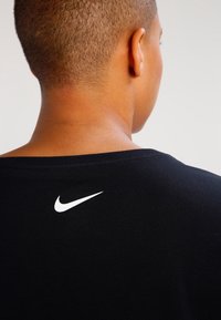Musta lyhythihainen t-paita pyöreällä kaula-aukolla, jossa on valkoinen Nike-logo yläselässä. Valmistettu pehmeästä, teksturoidusta materiaalista.