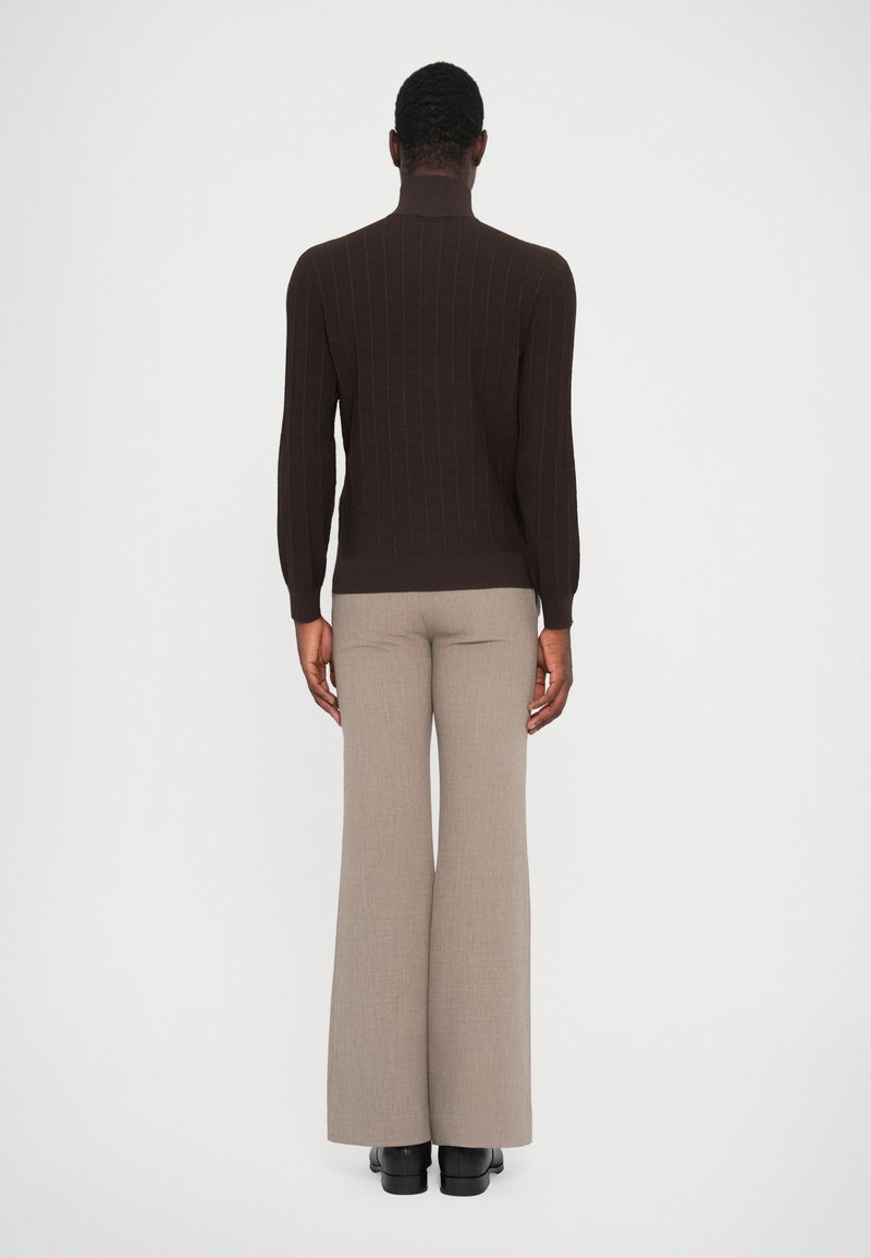 Mørkebrun ribbet højhalset sweater parret med beige flared bukser, der har et tekstureret stof og en skræddersyet pasform.