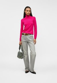 Bright pink turtleneck sweater, gray wide-leg jeans, brown belt, textured gray handbag, black pointed flats; smooth fabric and casual fit.
