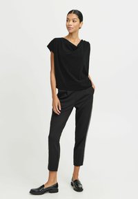 Top nero a maniche corte con scollo drappeggiato, abbinato a pantaloni neri su misura con strisce laterali e mocassini neri eleganti.
