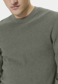 Pull en tricot vert olive avec un motif texturé côtelé. Présente un col rond et une silhouette ajustée, mettant en valeur un tissu doux et subtil.