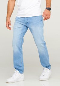 Ljusblå denimjeans med en avslappnad passform, som visar subtila blekningar. I kombination med vita sneakers och en enkel vit t-shirt.