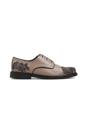 Beżowy skórzany elegancki but z czarną kwiatową haftowaną dekoracją na czubku i pięcie, czarne sznurowadła i czarna podeszwa, widoczny z boku.