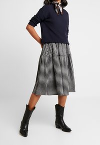 Granatowy sweter prążkowany w połączeniu z czarno-białą spódnicą w kratę o długości midi, z warstwowym krojem i czarnymi botkami sięgającymi za kolano.