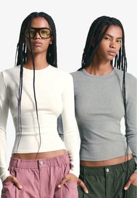 Topuri cu mâneci lungi din bumbac ecru și gri, cu gât rotund. Asortate cu pantaloni roz și verzi, cu șnur în talie.