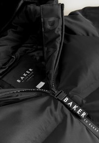 Juodas švarkas su lygiu paviršiumi, turintis ryškų užtrauktuką ir "BAKER" logotipą ant užtrauktuko traukimo. Viduje yra minkšta, matinė pamušalo medžiaga.