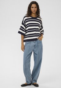 Marineblaues und weiß gestreiftes Baumwoll-T-Shirt mit weiten Ärmeln, kombiniert mit hellblauen hoch taillierten Jeans, dazu schwarze Ballerinas.