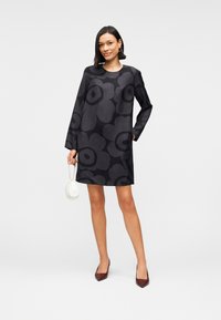 Μαύρο φόρεμα με λουλούδια, με μακριά μανίκια, στρογγυλή λαιμόκοψη και άνετη εφαρμογή. Διαθέτει λεπτό υφασμάτινο μοτίβο και συνδυάζεται με λευκή τσάντα.