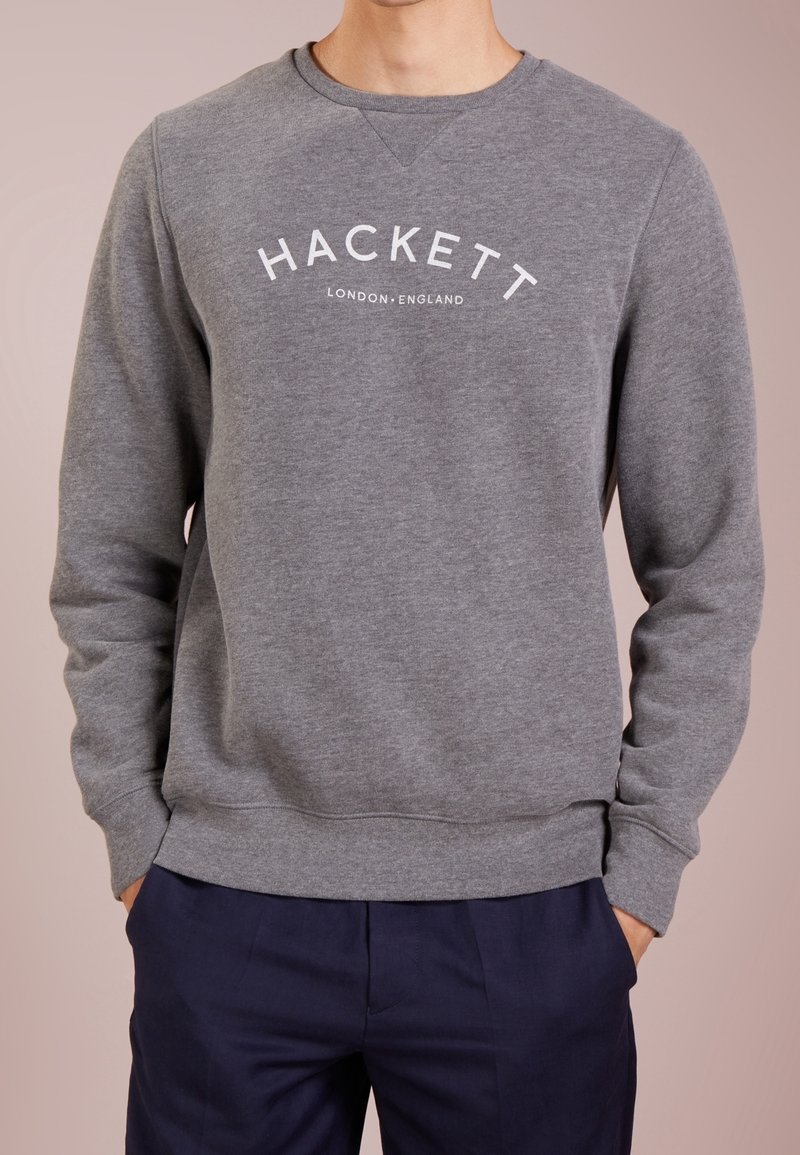 Sudadera gris con puños y dobladillo acanalados, que presenta un logo blanco de "Hackett London England" en el pecho. Textura de tela suave.