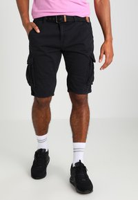 Mustat cargo-shorts, joissa on useita sivutaskuja, vyö ruskealla yksityiskohdalla, yhdistettynä valkoisiin sukkiin ja mustiin tennareihin.