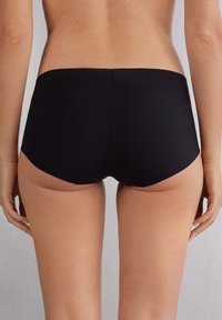 Černé pružné tkaninové hipster kalhotky s hladkým povrchem a bezešvými okraji, které se vyznačují klasickým designem a minimalisticé estetikou.