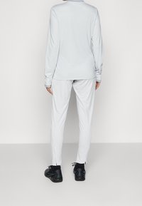 Světle šedý dlouhý rukáv top a odpovídající kalhoty se zipy na kotnících, doplněné černými sportovními botami. Hladký, elastický materiál.