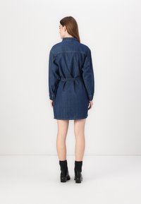 Abito in denim con maniche lunghe, vita cintrata e taglio dritto. Colore blu scuro, cuciture più chiare e un design classico del colletto.