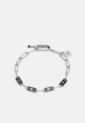 Bracciale in catena d'argento con anelli smaltati in bianco e nero che formano la scritta "DKNY." Include un piccolo tag circolare con il logo del marchio.