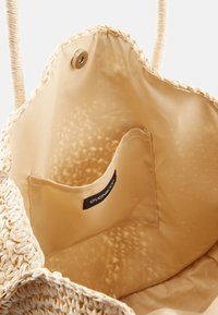 Vävd halm väska med en ljusbeige inredning, som har en liten ficka och knappstängning. Handtagen är prydda med en flätad textur.