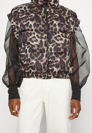 Kurtka typu puffer w panterkę z zamkiem z przodu, noszona na przejrzystej czarnej bluzce z bufkami na rękawach i białych spodniach z wysokim stanem.