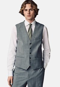 Chaleco gris texturizado con cinco botones negros, dos bolsillos frontales y cuello con muesca, usado sobre una camisa blanca y una corbata de patrón verde.
