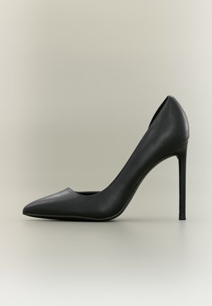 Chaussure stiletto noire en cuir à talon haut avec bout pointu sur un fond clair uni.
