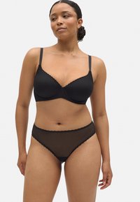 Sujetador negro con encaje en el borde y braguita transparente a juego con patrón de diamantes. La tela tiene un aspecto texturizado y el diseño incluye tirantes ajustables.