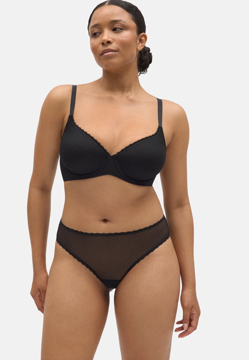Sujetador negro con encaje en el borde y braguita transparente a juego con patrón de diamantes. La tela tiene un aspecto texturizado y el diseño incluye tirantes ajustables.