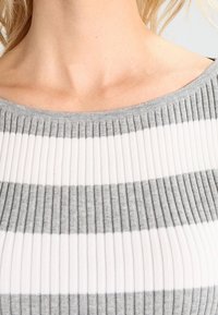 Maglietta a righe grigie e bianche con una texture a costine, scollatura ampia e tessuto morbido, con un focus sulle bande di colore alternate e sui sottili plissettature.