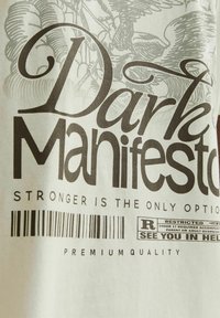 T-shirt bianca con un grande design grafico nero e testo che recita "Dark Manifesto" e dettagli del codice a barre. Materiale di cotone morbido.