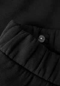 Detailopname van een zwarte elastische tailleband met een zwart knoopdetail op zachte, gevarieerde stof.