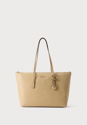 Sac fourre-tout en cuir couleur tan avec doubles bretelles et pendentif doré avec le logo Michael Kors suspendu à une bretelle.