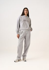 Világosszürke kapucnis pulóver "LAMANIA" sötétvörös felirattal, világosszürke nadrággal párosítva, lazított szabással és finom textúrával.