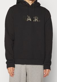 Sudadera negra con cordones, logo frontal B.A.L.R. con un acabado brillante, tejido suave, mangas largas y puños y dobladillo acanalados.