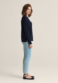 Mörkblå stickad tröja med avslappnad passform, matchad med ljusblå skinny jeans och svarta lägenheter med ankelremmar. Minimal design och struktur.