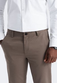Bruine broek van textuurstof met een rechte snit, voorzien van een enkele knoopsluiting en zijzakken, gedragen met een witte shirt.