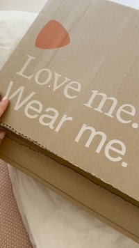 Braune Pappschachtel mit weißem Text "Love me. Wear me." und einem kleinen roten dreieckigen Logo auf dem Deckel.