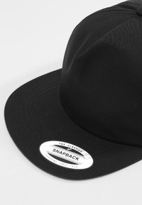 Zwarte snapback pet met een gestructureerde kroon en een rechte vizier. Voorzien van een ronde witte label met de merknaam en het jaar. Gelaagd textiel.