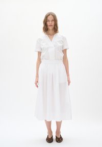 White, short-sleeved dress with a V-neck, gathered waist, and a flowing, sheer skirt. Worn with animal print flats.