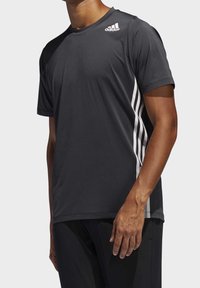 Sportovní tričko s krátkým rukávem v tmavě šedé barvě, vyrobené z lehké tkaniny. Obsahuje bílé logo Adidas a tři bílé pruhy po stranách.