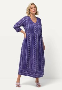 Valkoinen ja violetti kuviollinen maksimekko, jossa on 3/4-hihat, V-pääntie ja gathered vyötärö. Mekossa on kukka- ja geometrisia kuvioita, jotka eroavat voimakkaasti valkoisesta.