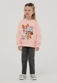 Felpa rosa chiaro con illustrazioni di cani giocosi e la scritta "Buona giornata!", abbinata a jeans grigi e sneaker argentate.