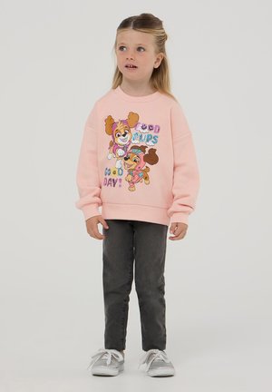 Felpa rosa chiaro con illustrazioni di cani giocosi e la scritta "Buona giornata!", abbinata a jeans grigi e sneaker argentate.