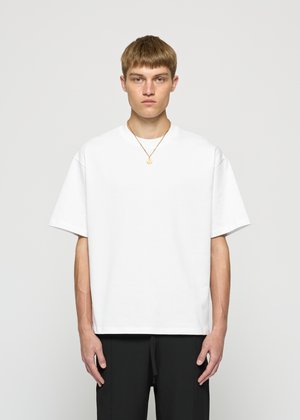 White oversized cotton t-shirt with a round neckline and short sleeves, featuring a smooth texture and minimalistic design.
