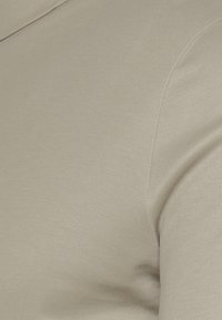 Tessuto di cotone beige con una texture liscia; messa a fuoco ravvicinata sulla trama del materiale e sull'aspetto morbido. Taglio regolare senza motivi o accenti visibili.