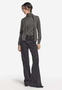 Grå polokragetröja i kombination med hög midja mörka jeans med utsvängda ben. Tröjan har långa ärmar och outfiten kompletteras av svarta skor.