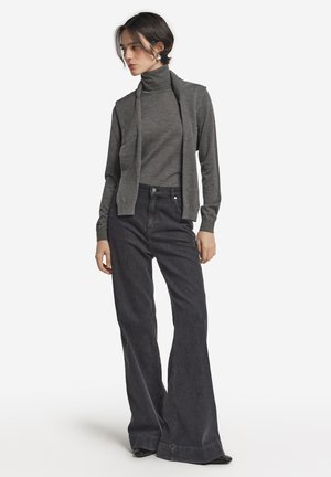 Grauer Rollkragenpullover kombiniert mit hochgeschnittenen, dunkelblauen, ausgestellten Jeans. Der Pullover hat lange Ärmel, und das Outfit wird mit schwarzen Schuhen ergänzt.