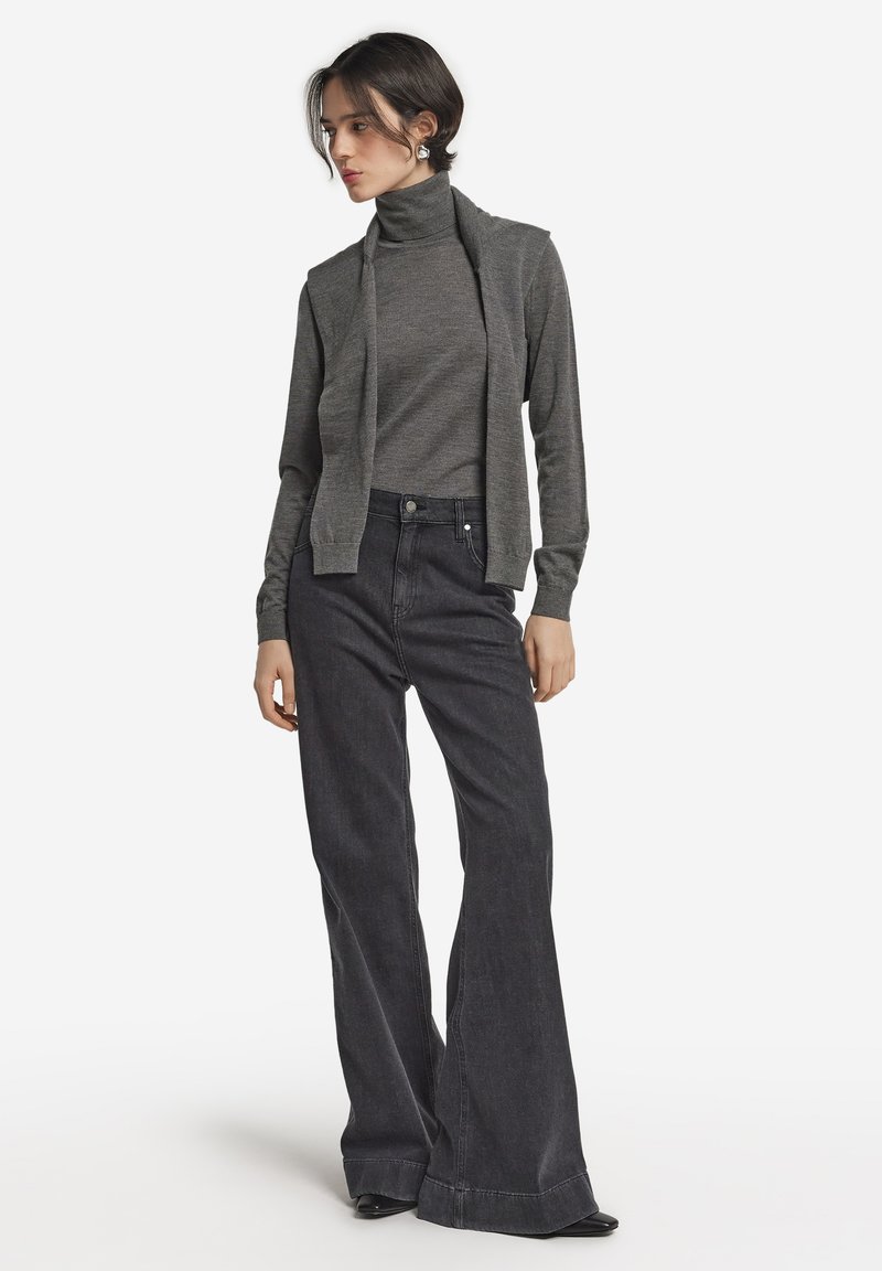 Grå polokragetröja i kombination med hög midja mörka jeans med utsvängda ben. Tröjan har långa ärmar och outfiten kompletteras av svarta skor.