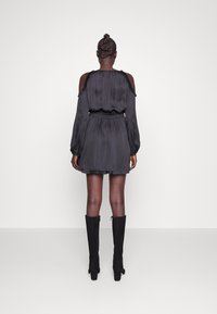 Svart sidenklänning med off-shoulder ärmar, volangdetaljer och en figursydd midja. Kombinerad med knähöga svarta stövlar.