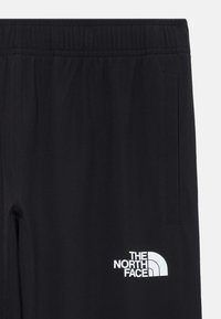 Calças de desporto pretas com um cós elástico, bolsos laterais e um logo branco na coxa esquerda. Tecido suave com um acabamento mate.
