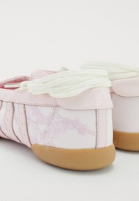Ténis de atletismo cor-de-rosa com padrão floral bordado, laterais em malha, solas de borracha e atacadores brancos. Logótipo da marca no calcanhar. Design arredondado.